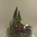 Model of a construction site with trees and rocks inside a glass container.