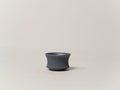 A gun metal teacup-shaped plant pot with a wide mouth on a plain background.