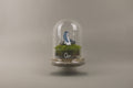 Small model of a person sitting on grass under a glass dome with a brand logo. Custom terrariums for Nike